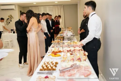 Lungo buffet salato in sala con vassoi di antipasti, tramezzini, salumi, rustici e piatti caldi disposti su più livelli. Gli ospiti sono in fila lungo il tavolo mentre il personale di servizio resta ai lati, in un ambiente luminoso con pareti neutre e pavimento chiaro.