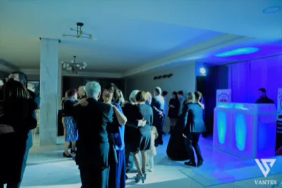 Ospiti che ballano in coppia nella sala interna durante una festa serale, con illuminazione blu e viola proveniente dalla consolle DJ sulla destra. L'ambiente ha pavimento lucido, pilastri chiari e un'atmosfera raccolta da ricevimento con musica dal vivo o intrattenimento in sala.