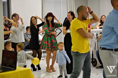 Momento di animazione in sala con adulti e bambini coinvolti in un ballo di gruppo durante la festa. L'immagine mostra un'atmosfera informale e vivace, con ospiti in piedi, bambini in primo piano e area interna luminosa dedicata all'intrattenimento.