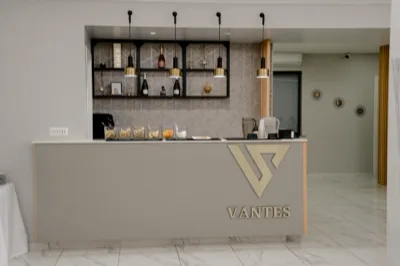 Banco bar interno della sala con linee minimal, bottiglie esposte su scaffalature retroilluminate e piccoli snack e bevande sul piano. L'ambiente è luminoso, ordinato e pensato per il servizio drink durante l'evento.