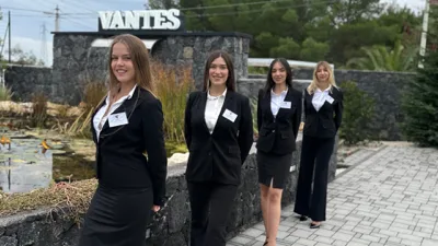 Quattro donne dello staff Vantes in abito nero e camicia bianca posano all'esterno vicino all'ingresso con insegna VANTES e laghetto sullo sfondo. La scena mostra il team in divisa in un contesto naturale e ordinato, con pavimentazione in pietra e area verde attorno.