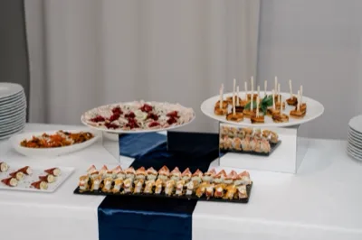 Tavolo buffet assortito con involtini, pinse, salumi, insalate, piccoli monoporzione e tartine disposti su alzate nere e bianche. La scena è un primo piano ricco di portate diverse, con una presentazione ordinata e luminosa da catering.