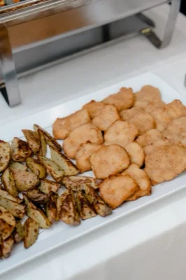 Vassoio con fritti dorati e patate al forno serviti come secondo o contorno al buffet, ripresi molto da vicino. La preparazione è su piatto bianco e mostra una presentazione semplice ma curata da servizio catering.
