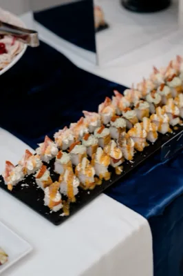 Vassoio nero con finger food tipo sushi o piccoli canapè disposti in file ordinate, decorati con salse chiare e arancioni. La composizione è molto ravvicinata e mostra una presentazione elegante da buffet serale.