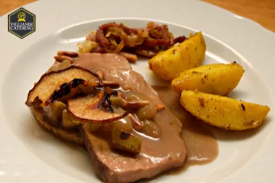 Piatto di carne servito con salsa cremosa, patate al forno e contorno di frutta e verdure saltate, ripreso in primo piano su piatto bianco. La presentazione è curata e valorizza una proposta di secondo piatto dal taglio più classico.