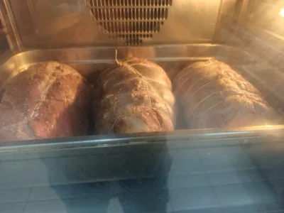 Tre arrosti legati cuociono in forno dentro una grande teglia metallica, ripresi attraverso il vetro dell'elettrodomestico. L'immagine documenta una fase di cottura della carne nelle preparazioni di Viglianisi Catering.