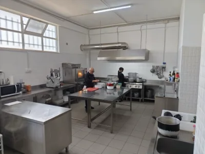 Vista ampia della cucina professionale di Viglianisi Catering, con cuochi al lavoro tra fornelli, banco inox, pentole e attrezzature. L'immagine racconta l'organizzazione del laboratorio in una fase di preparazione operativa.