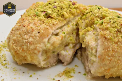 Preparazione farcita e gratinata servita in trancio, con interno cremoso visibile al taglio e copertura di pistacchio tritato sulla superficie. Il primo piano mette in risalto la consistenza ricca del ripieno e la doratura della panatura esterna.