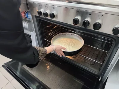 Tortiera con composto chiaro appena inserita nel forno, in una fase di cottura del pan di Spagna. La foto documenta un momento operativo del laboratorio di pasticceria di Viglianisi Catering.