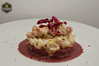 Risotto impiattato in forma cilindrica su una salsa violacea, con topping cremoso e foglie di radicchio come guarnizione. La presentazione è elegante e minimal, pensata per valorizzare un primo piatto dal taglio più raffinato.