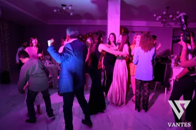 Festa a tema ballo in sala interna, con ospiti che danzano sotto una luce magenta intensa e un fotografo che riprende la scena. Sullo sfondo si intravedono tavoli allestiti e palloncini per la festa.
