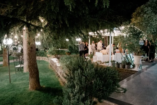 Pagoda in giardino di sera circondata da alberi, luci sospese e vegetazione curata, con ospiti riuniti sotto la copertura. L'ambiente comunica un evento elegante e raccolto all'aperto.