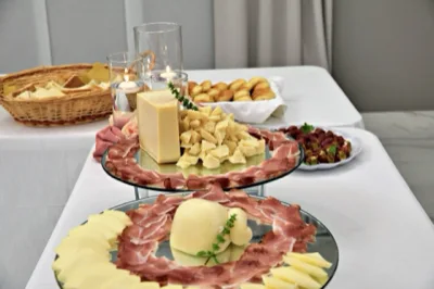 Angolo buffet con salumi e formaggi disposti su alzate a specchio, affiancati da pane, grissini e piccoli assaggi sullo sfondo. L'allestimento unisce presentazione decorativa e varietà di prodotti per il momento aperitivo o buffet.