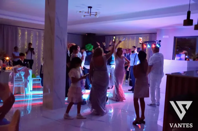 Serata di ballo in sala con invitati in pista, luci colorate e postazione DJ sullo sfondo. L'immagine trasmette un momento vivace di festa con atmosfera serale e intrattenimento musicale.