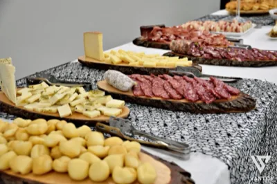 Buffet di salumi e formaggi allestito su taglieri rustici, con pinze da servizio, formaggi a cubetti, salami affettati e piccoli panini in primo piano. La composizione mette in evidenza la cura dell'angolo catering e la varietà della proposta salata.