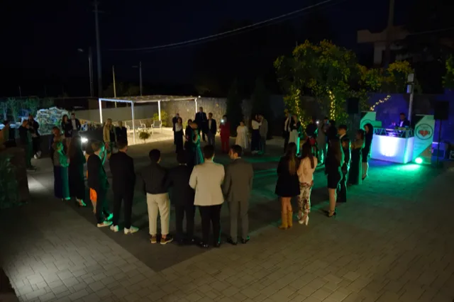 Ospiti disposti in cerchio nello spiazzale esterno durante un momento di animazione o ballo serale, con illuminazione verde e DJ set acceso sulla destra. Sullo sfondo si vedono il pergolato lounge, il laghetto e le luci decorative della location.