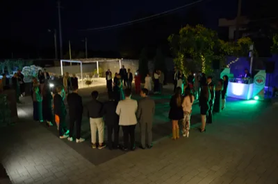 Ospiti disposti in cerchio nello spiazzale esterno durante un momento di animazione o ballo serale, con illuminazione verde e DJ set acceso sulla destra. Sullo sfondo si vedono il pergolato lounge, il laghetto e le luci decorative della location.