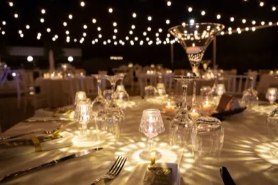 Tavolo apparecchiato con dettagli luccicanti e mise en place elegante per un ricevimento, con bicchieri, posate e centrotavola raffinato in un ambiente luminoso.