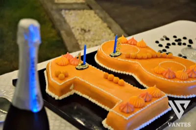 Torta a forma di numero 18 color arancio, decorata con piccole meringhe, sfere dolci e candeline blu. La presentazione è semplice ma d'effetto, pensata per una festa di diciottesimo compleanno.