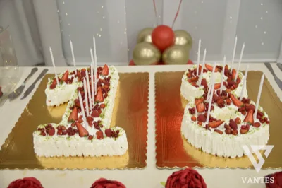 Torta a forma di numero 18 decorata con panna, fragole, frutti rossi e candeline bianche, servita su due basi dorate separate. La presentazione è fresca e festosa, ideale per un diciottesimo compleanno.