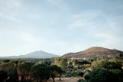 Panorama aperto con vista sull'Etna e sulle colline circostanti, tra alberi, campagna e cielo chiaro. L'immagine valorizza il contesto naturale che circonda la location.